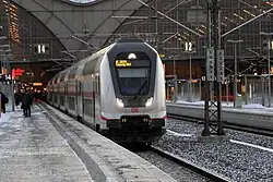 Barevná fotografie s pohledem na dvoupatrový vlak přijíždějící na nádraží