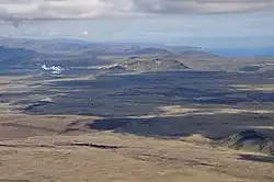Pohled na rozsáhlá lávová pole. V pozadí hora Þorbjörn, geotermální elektrárna Svartsengi a geotermální lázně Blue Lagoon.
