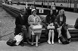 Lidé sedící na konci koleje 8 na nádraží v Helsinkách. Cestující čekající na vlak na nástupišti v pozadí. 1971.