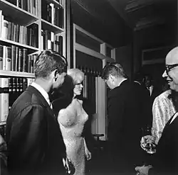 Prezident John F. Kennedy (zády k fotoaparátu), americký generální prokurátor Robert Kennedy (zcela vlevo) a herečka Marilyn Monroe, u příležitosti 45. narozenin prezidenta Kennedyho na Madison Square Garden v New Yorku. Arthur M. Schlesinger je vzadu vpravo, vzadu je zpěvák Harry Belafonte, 19. května 1962.