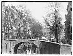 Warmoesgracht 2 t/m 26 (v.r.n.l.) (na 1895: Raadhuisstraat). Gezien van de Herengracht richting Singel en het Koninklijk Paleis. Op de voorgrond is brug nr. 22; 1894.