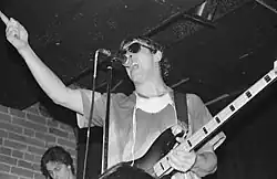 Zpívající muž stojící před mikrofonem, v ruce drží bassovou kytaru.