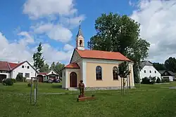 Náves s kapličkou a sochou dřevaře