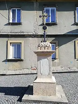 Detail kamenného sloupku s litinovým krucifixem před objektem (rok 2022)