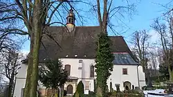 Fotografie zachycuje kostel mezi stromy v areálu hřbitova