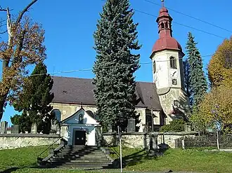 Jižní průčelí kostela s předsíní a věží, oprýskaná fasáda, v popředí stromy