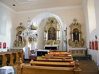 Pohled do interiéru: v popředí lavice, v pozadí presbytář s hlavním oltářem, kazatelnou, vedlejší oltáře