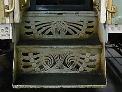 Dva dřevěné schody, které jsou zezadu a z obou boků uzavřeny kovovými deskami. Do zadních desek jsou vyřezány secesní motivy.