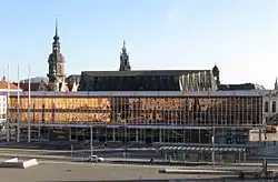 Barevná fotografie na moderní budovu ve stylu brutalismu, za níž ční dvě věže