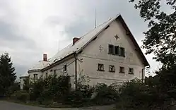 Zděný dvoupatrový dům, před ním zelené stromy a keře.