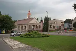 Náves v kunraticích. V pozadí domy, v centru přízemní kulturní dům, za ním patrná věž kostela.