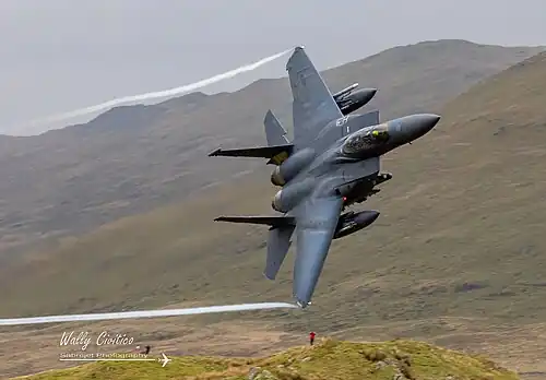 F-15E Strike Eagle amerického letectva základnou v Lakenheathu v hrabství Suffolk, v pozadí několik spotterů, 2022