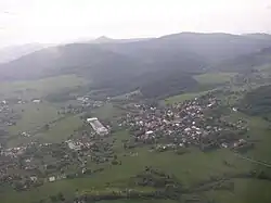 Letecký pohled na část Lužických hor; v popředí Jiřetín pod Jedlovou obklopený lukami, v pozadí zalesněná krajina: zleva Weberberg, údolí Milířky, Luž a Pěnkavčí vrch