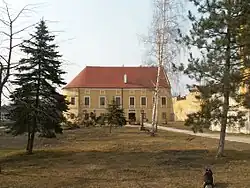 V pozadí budova muzea, před níž se nachází malý parčík s několika stromy a s božími mukami.