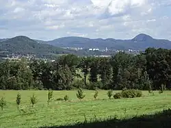 Prosluněný letní pohled od České lípy z polí pod vrcholy na panorama Lužických hor, kde souvislý lesní porost místy přerušují lidská sídla