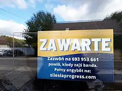 Tabulka s nápisem „ZAVŘENO. Zavolejte na 693 953 661, řeknu, kdy tu zase budu. Úplná nabídka na silesiaprogress.com“ ve výloze obchodu v Luboszycích u Opolí