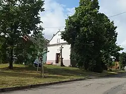 Podlouhlá mírně svažitá náves se vzrostlými stromy a kaplí