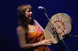 Fotografie ženy s mikrofonem, držící buben