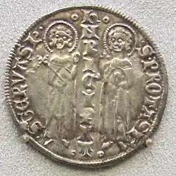 Lehce setřená mince, na níž se nachází nápis a dvě postavy se svatozářemi.