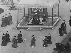 Císař sedící na stoličce v malém pavilónu sleduje skupin eunuchů kopající si míčem.