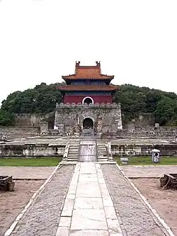 Fotografie několikapatrové stavby s charakteristickými střechami se zdviženými rohy, v pozadí zalesněný kopec, v popředí kamenná přístupová cesta