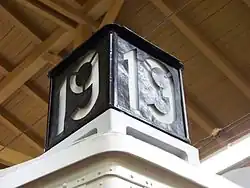 Černý budník s bíle vyvedeným číslem linky (19) posazený na rohu střechy tramvaje.