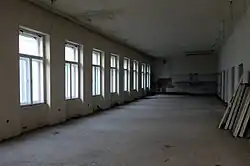 Fotografie velké místnosti přístupné z tanečního sálu. Po levé straně je osm rozměrných oken směřujících do Divadelní ulice. Místnost má poškozené omítky, chybí také lustry a topení.