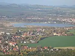 Barevná fotografie zalesněné a zčásti osídlené krajiny v jejímž středu se nachází jezero Olbersdorf
