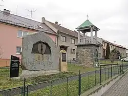 Dlouhá mírně svažitá náves s pomníkem obětem světových válek a zvonicí Československé církve husitské