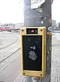 Přihlašovací zámek tramvajové signalizace. Svítící šipky zobrazují směry, do nichž je registrován aktuální nárok na signál pro jízdu. Jiné směry může řidič přihlásit čtyřhrannou kličkou z dolní části krabičky.