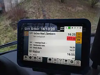 Palubní počítač pro řidiče ve vozidle hromadné dopravy ukazuje aktuální čas nadjezdu nad jízdním řádem s odstupem +11 minut.