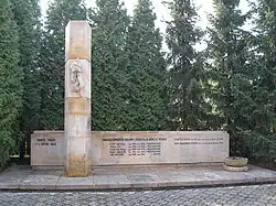 Kamenný památník (ve tvaru ležatého kvádru) uctívající oběti německé okupace stojící na nízkém vydlážděném podstavci v zátiší před jehličnatými stromy. V levé části pomníku je před pomník vystupující kameninový pilíř (dosahující asi trojnásobné výšky oproti ostatním prvkům pomníku), na kterém je plastika sepnutých rukou. Vlevo před památníkem je na kameninové základně kameninová miska.