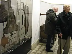 Rekonstrukce mučírny v Petschkově paláci v Praze. Vlevo předměty používané k mučení a vynucování výpovědí, v pozadí „hrazda“, na níž byli vězni různými způsoby zavěšováni. Křeslo pod hrazdou pro vyšetřovatele je původní.