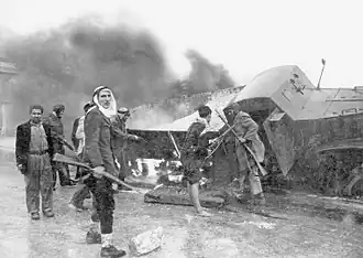 Palestinští bojovníci před hořícím obrněným zásobovacím vozem Hagany poblíž Jeruzaléma (březen 1948)