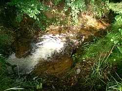 Pohled na odtékající Bělský potok padající z potrubí od propusti.