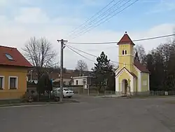 Náves s kapličkou svatého Bartoloměje, v pozadí železniční zastávka