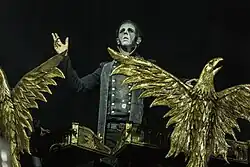 Klávesista skupiny Powerwolf Falk Maria Schlegel během koncertu v roce 2018. Maria Schlegel stojí za varhany zdobenými pozlacenými orly, nehraje, nýbrž gestikuluje rukama jako kdyby kázal.