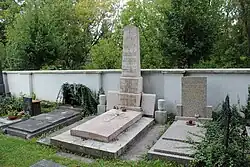 Kamenný pomník ze světlého kamene vybudovaný u hřbitovní zdi.