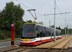 Moderní nízkopodlažní tramvaj typu Škoda 15T6 stojí ve stanici „Malešická továrna“.