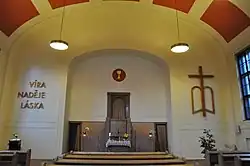 Kazatelna z umělého mramoru umístěná v nice. Po její levé straně jsou na zdi patrná tři slova, a sice „Víra“, „Naděje“ a „Láska“. Napravo od kazatelny se na zdi nachází dřevěná skulptura kříže a otevřené Bible.