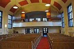 Pohled do sálu se třemi řadami lavic, v pozadí je patrná kruchat a na ní po levé i pravé straně varhanní píšťaly.