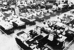 Interiér kanceláře Prológicy. Jde o otevřenou kancelář, bez žádných oddělovacích stěn mezi pracovišti. Fotografie je černobílá.