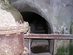 Pohled do interiéru chodby. Vlevo je vidět kovový uzávěr, v pozadí je vstup do chodby, jíž je vedena kovová roura.