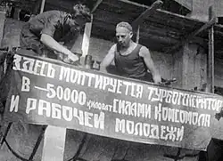 Na staveništi elektrárny Šaturskaja. Nápis na plakátu: „Sílami komsomolu a pracující mládeže se zde montuje turbogenerátor o výkonu 50 000 kilowattů.“ Rusko, Moskevská oblast, 1931