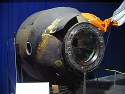 Zrezlý přistávací modul tvaru oblého komolého kužele ležící na boku.