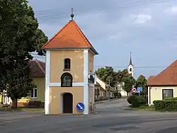 Zvonice na návsi v Rychmanově, v pozadí evangelický kostel