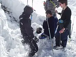 Na fotografii je několik osob ve sněhu, jedna osoba je částečně zasypaná.