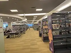 Interiér Národní knihovny Singapuru. Knižní police se sbírkami a čtenáři sedící u několika stolů.