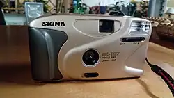 Skina SK-107 (Japonsko, 1990) – kinofilmový fotoaparát, používá pevně zaostřený objektiv