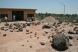 Kamenitá plocha s trojicí vědců v pozadí a červenou půdou